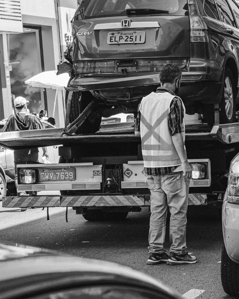 Operador ao lado de um guincho plataforma com um carro carregado, em foto preto e branco